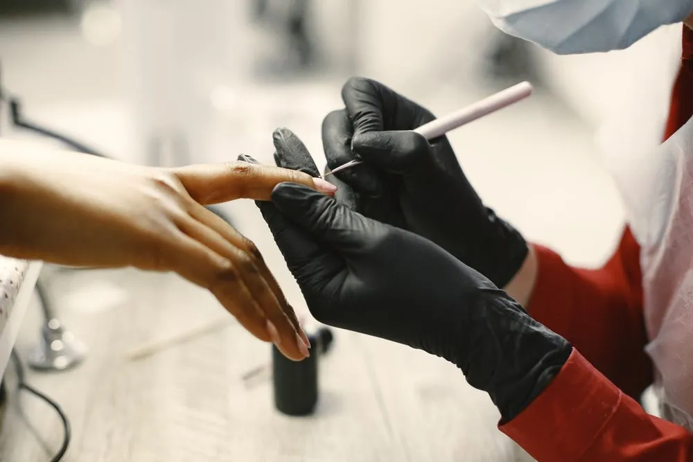 A nail technician in black gloves performing a manicure